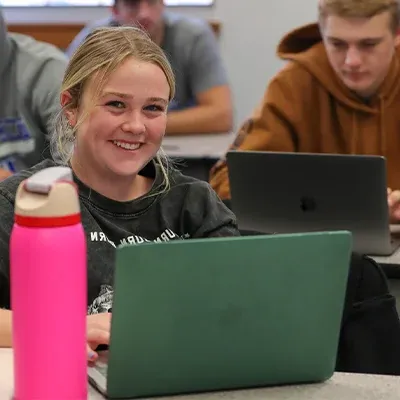 a student sitting in front of a laptop smiles at the camera